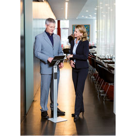 Ein Mann und eine Frau in Businesskleidung stehe vor einer Tablethalterung mit Bodenständer